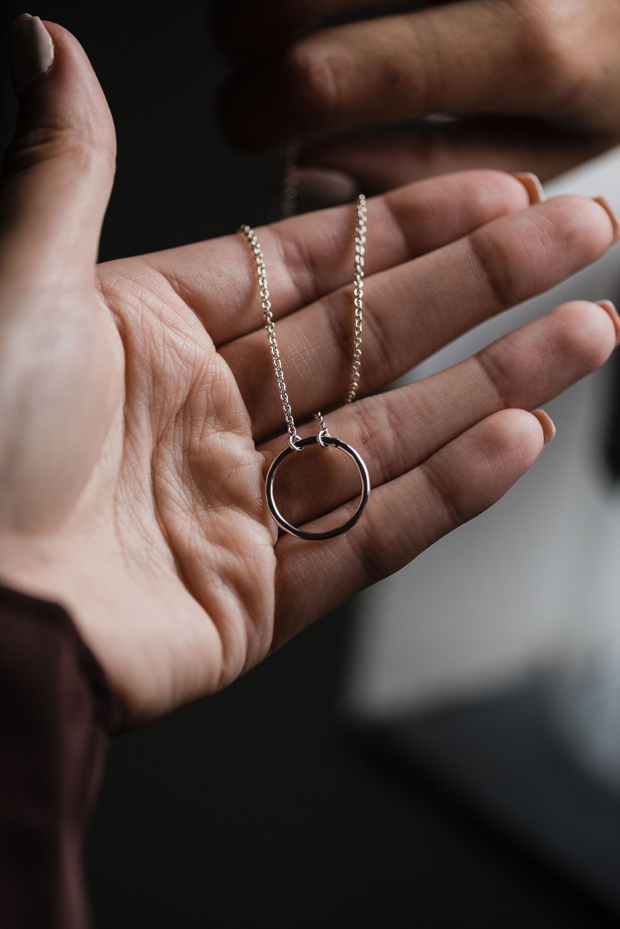 A model shot of a hand presenting our bestselling briony circle hammered necklace in silver with a delicate chain 