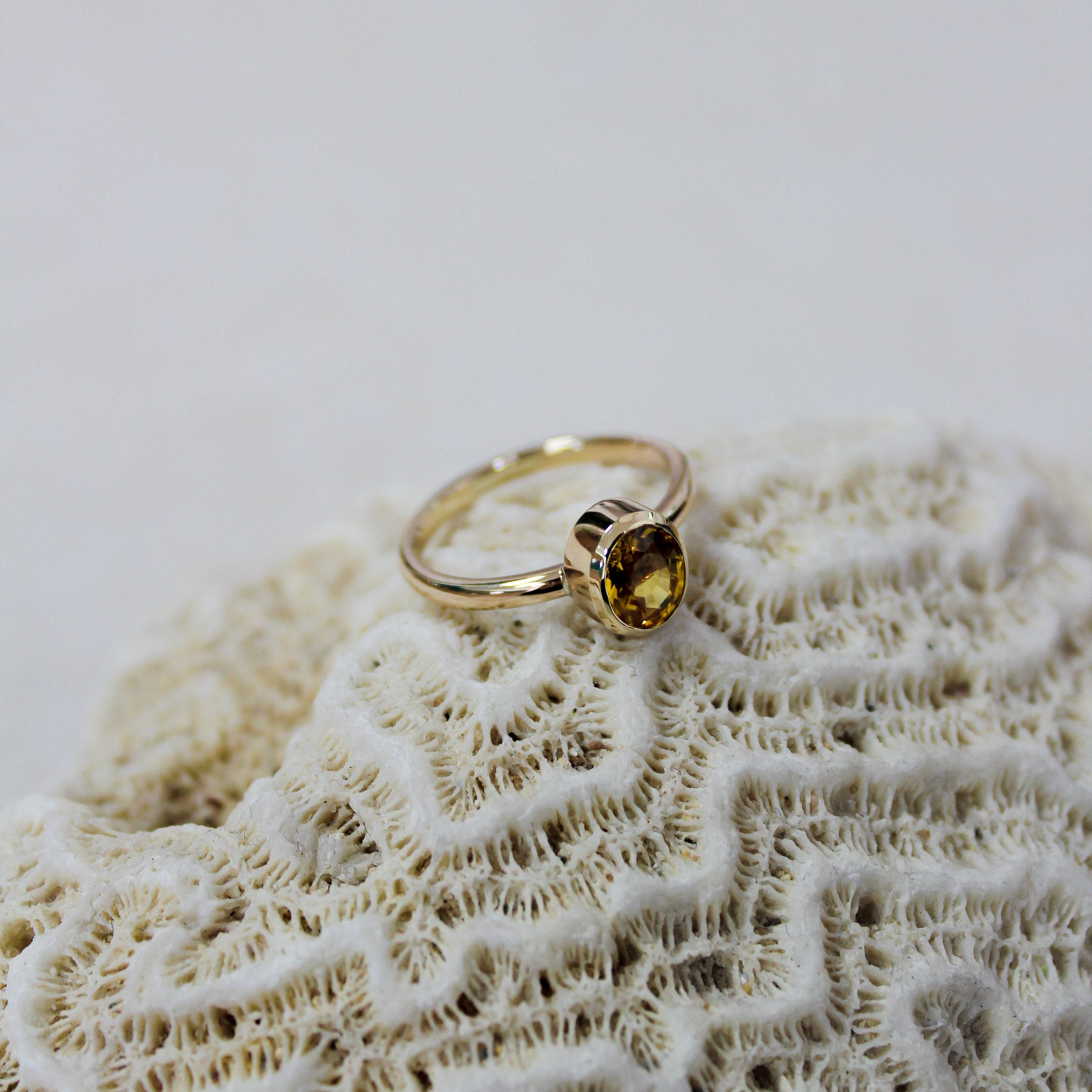 Gold ring with a yellow gemstone on a textured beige surface