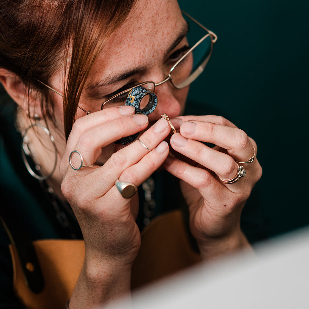 Person examining a small object with a magnifying glass against a dark background